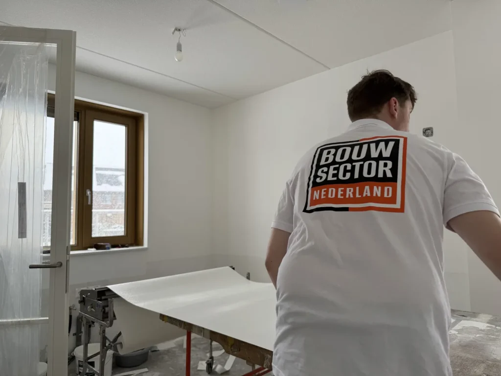 Behanger van Bouwsector Nederland in een wit shirt met logo trekt een baan vlies over de plaktafel naar de muur
