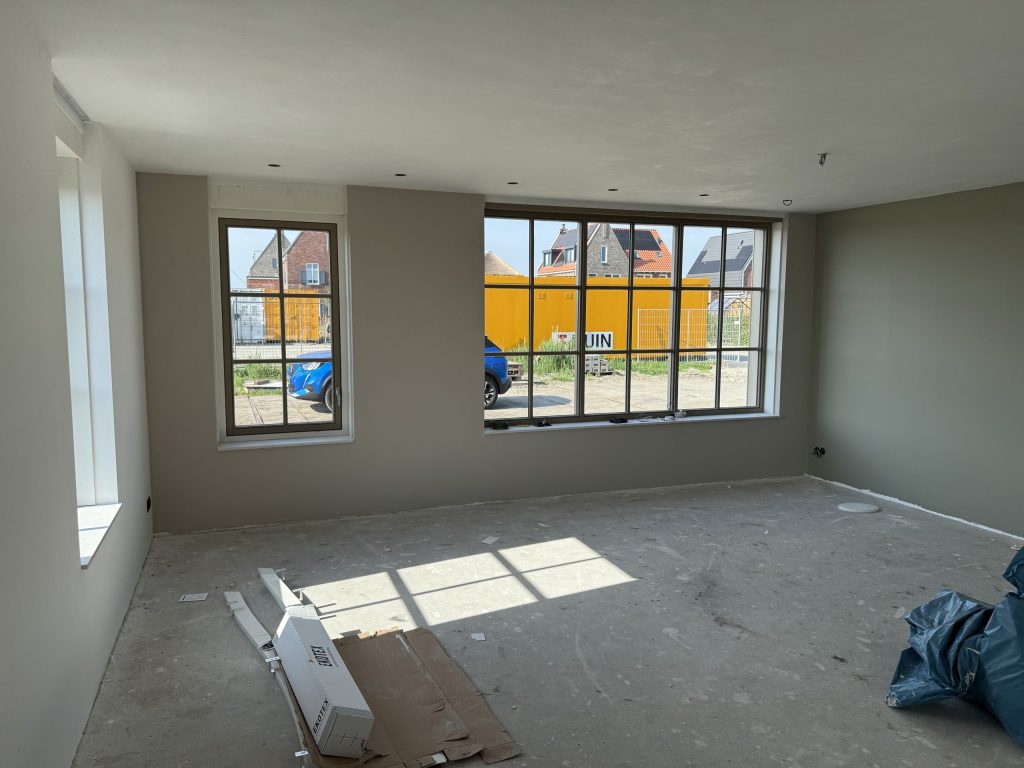 Ruime kamer op de begane grond van een nieuwe woning met wanden in een warme grijstint en grote ramen