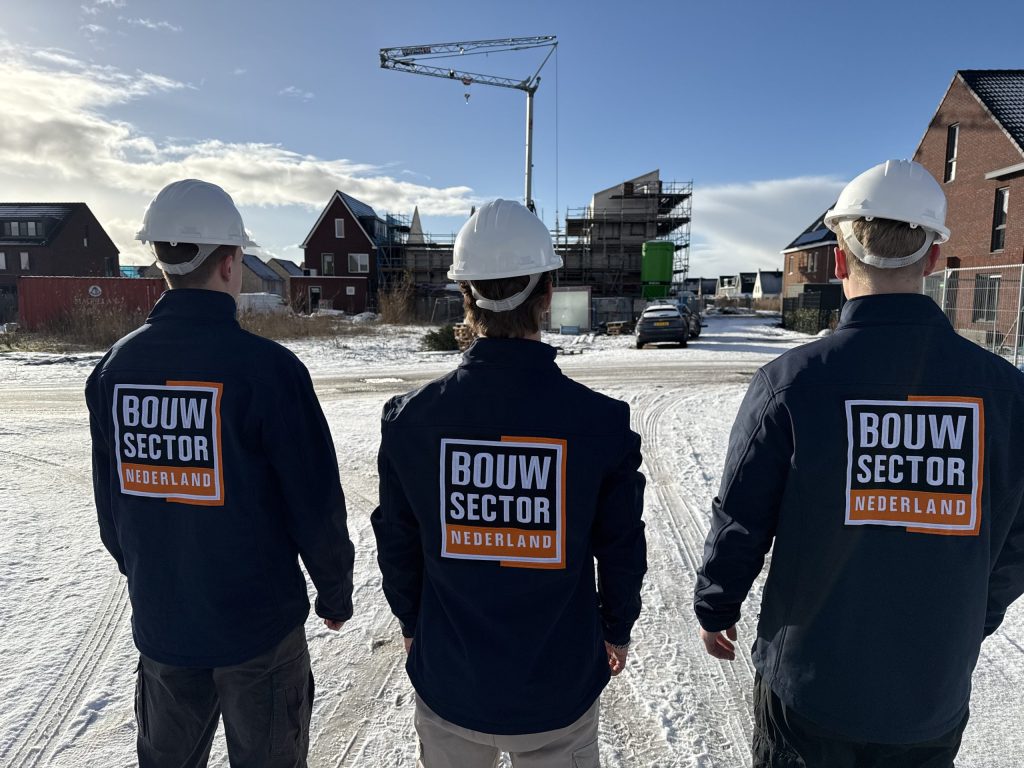 Drie vakmensen van Bouwsector Nederland met witte helm op een besneeuwde bouwplaats met een bouwkraan
